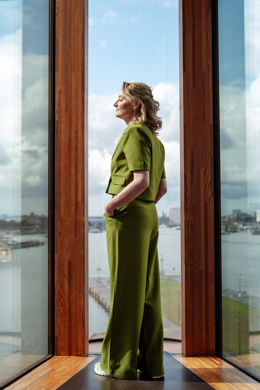 Dian in een groene outfit bij het raam, met uitzicht over de stad