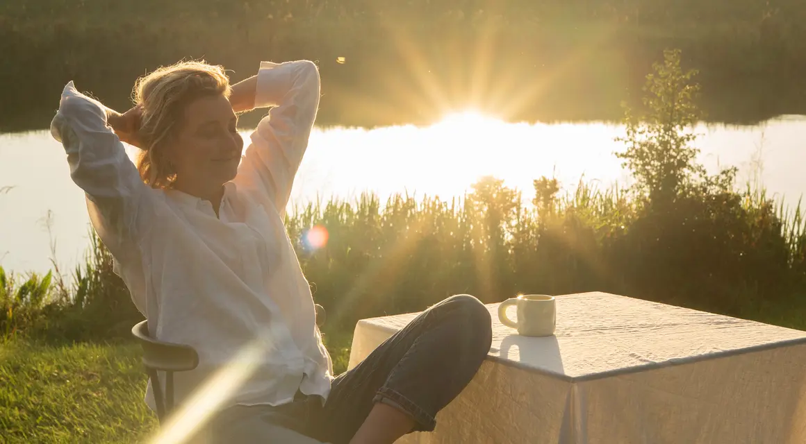 Dian leunt ontspannen achterover aan een tafel bij het water in de avondzon
